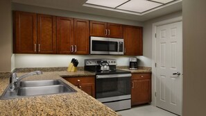 Una cocina con encimeras de granito, electrodomésticos de acero inoxidable, armarios de madera y una puerta blanca.