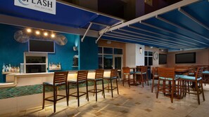 Un bar junto a la piscina con taburetes de madera y una barra que exhibe botellas.