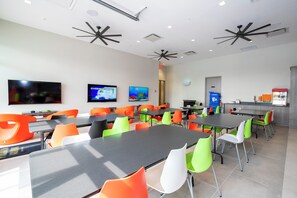 Un comedor moderno con varias mesas y sillas, ventiladores de techo y un televisor en la pared.