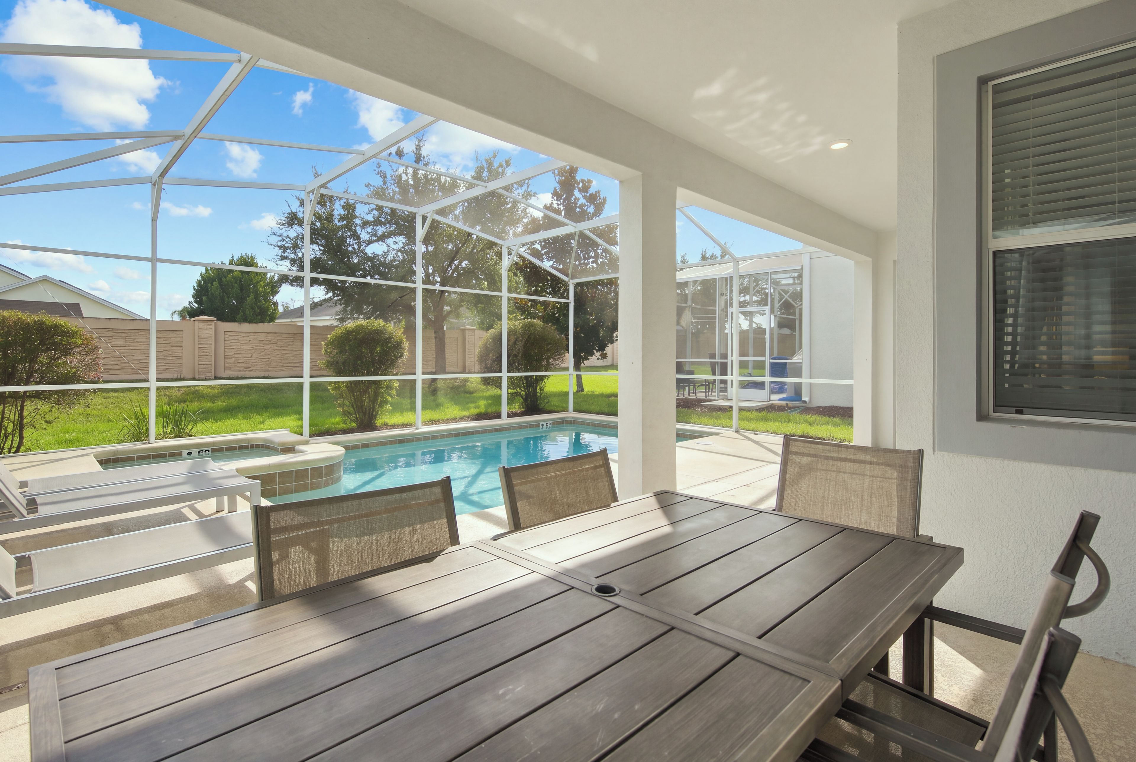 Une terrasse couverte avec une piscine, du mobilier d’extérieur et une vue sur le jardin arrière.