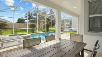 Une terrasse couverte avec une piscine, du mobilier d’extérieur et une vue sur le jardin arrière.