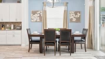 Un coin repas avec une table et des chaises, une cuisine à l’arrière-plan et une fenêtre avec des rideaux.