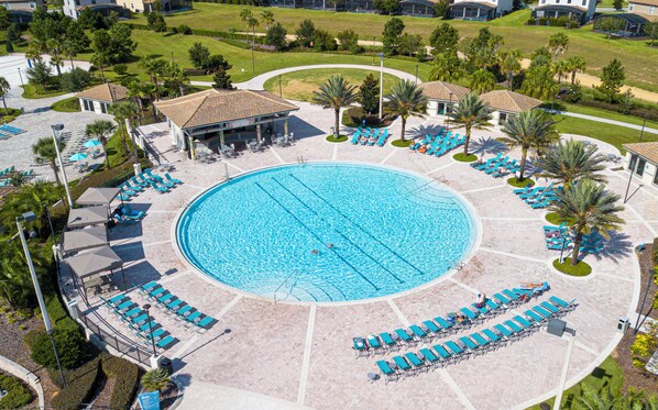 Luftaufnahme eines Resorts mit einem zentral gelegenen Schwimmbad, Liegestühlen und Palmen.