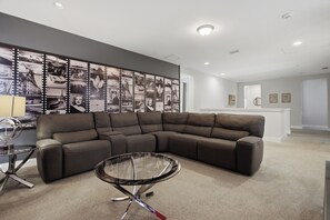 Ein modernes Wohnzimmer mit einer Eckcouch, einem Glastisch und einer Wand mit einer Fotocollage im Filmstreifen-Stil.
