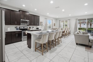 A modern kitchen with dark cabinets, stainless steel appliances, and a central island with bar stools. - Prime Location Near Disney with Private Theater (Kissimmee)