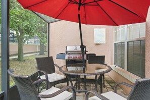An outdoor patio with wicker chairs, a round table, a red umbrella, and a barbecue grill. - Star Wars & Mickey Kids Rooms | 18 Min to Disney (Kissimmee)