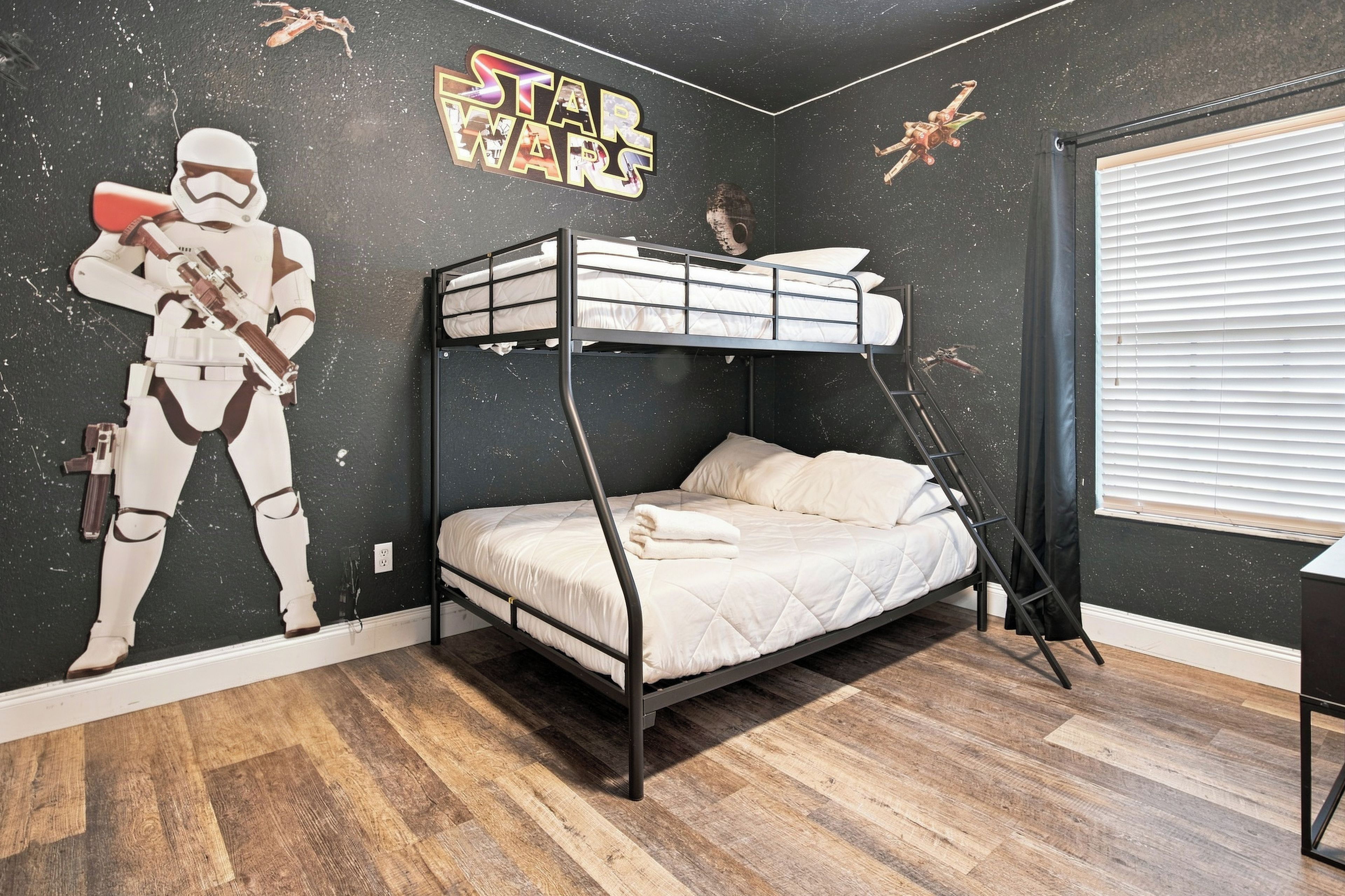 Ein Schlafzimmer mit Etagenbett und Wandbildern zum Thema Star Wars, einem Fenster mit Jalousien und einem Holzboden.