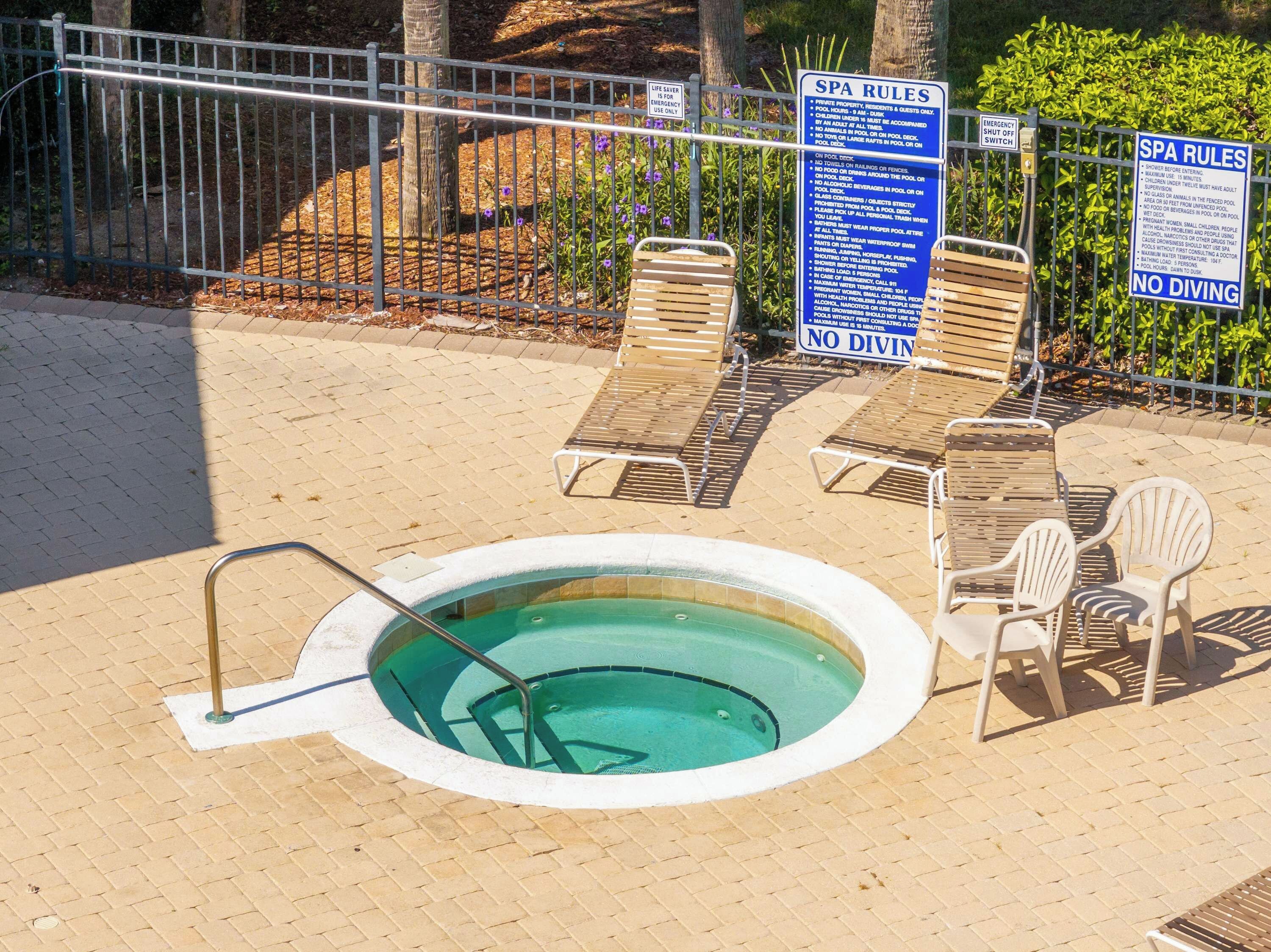Ein kleiner, runder Whirlpool umgeben von Liegestühlen, mit einem Schild, das Spa-Regeln und ein Sprungverbot anzeigt.