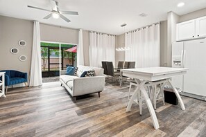 A modern living room with a sofa, dining table, and kitchen area. - Star Wars & Mickey Kids Rooms | 18 Min to Disney (Kissimmee)