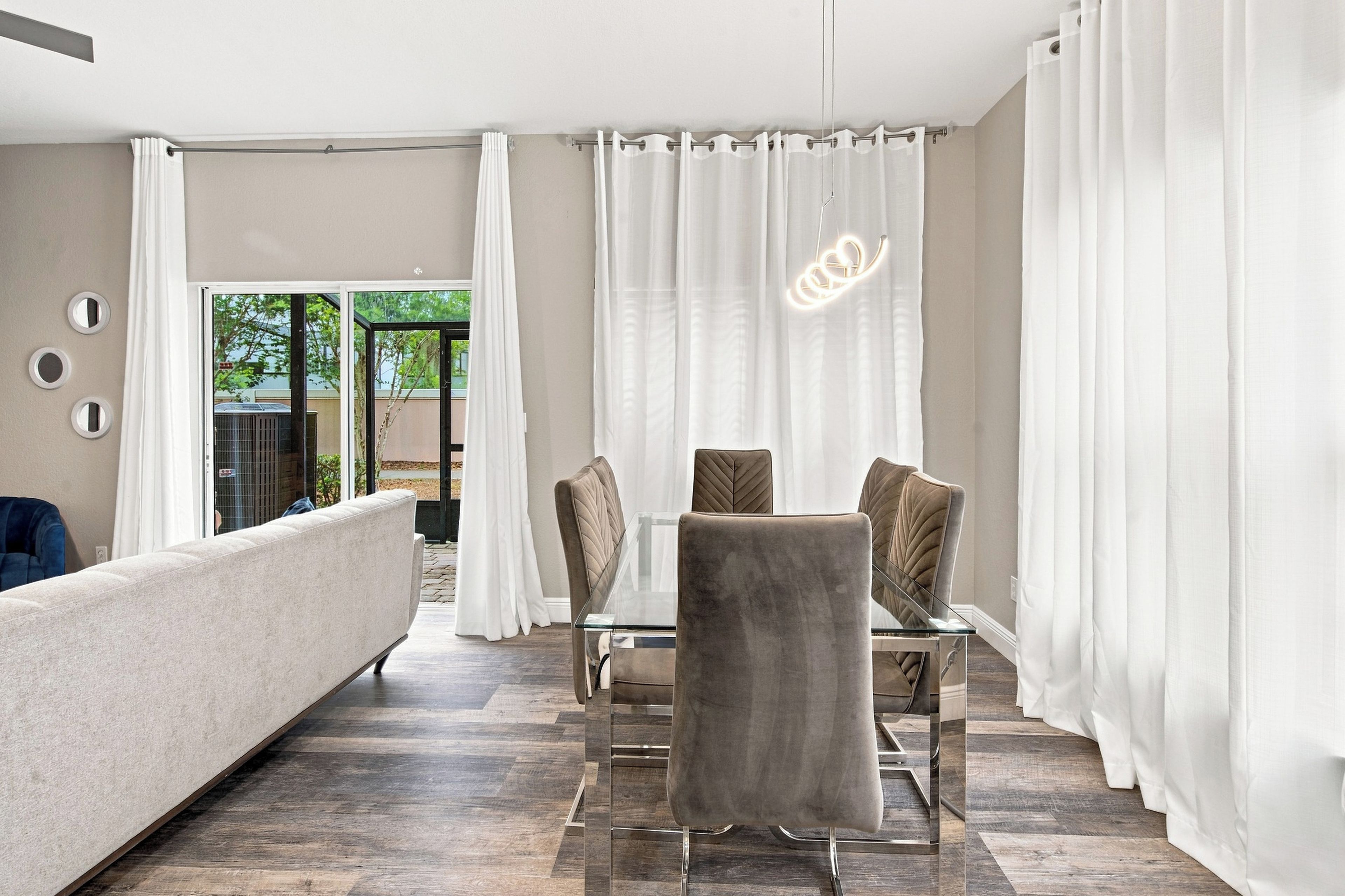 A modern living room with a sofa, a dining table with chairs, and a view through a glass door.