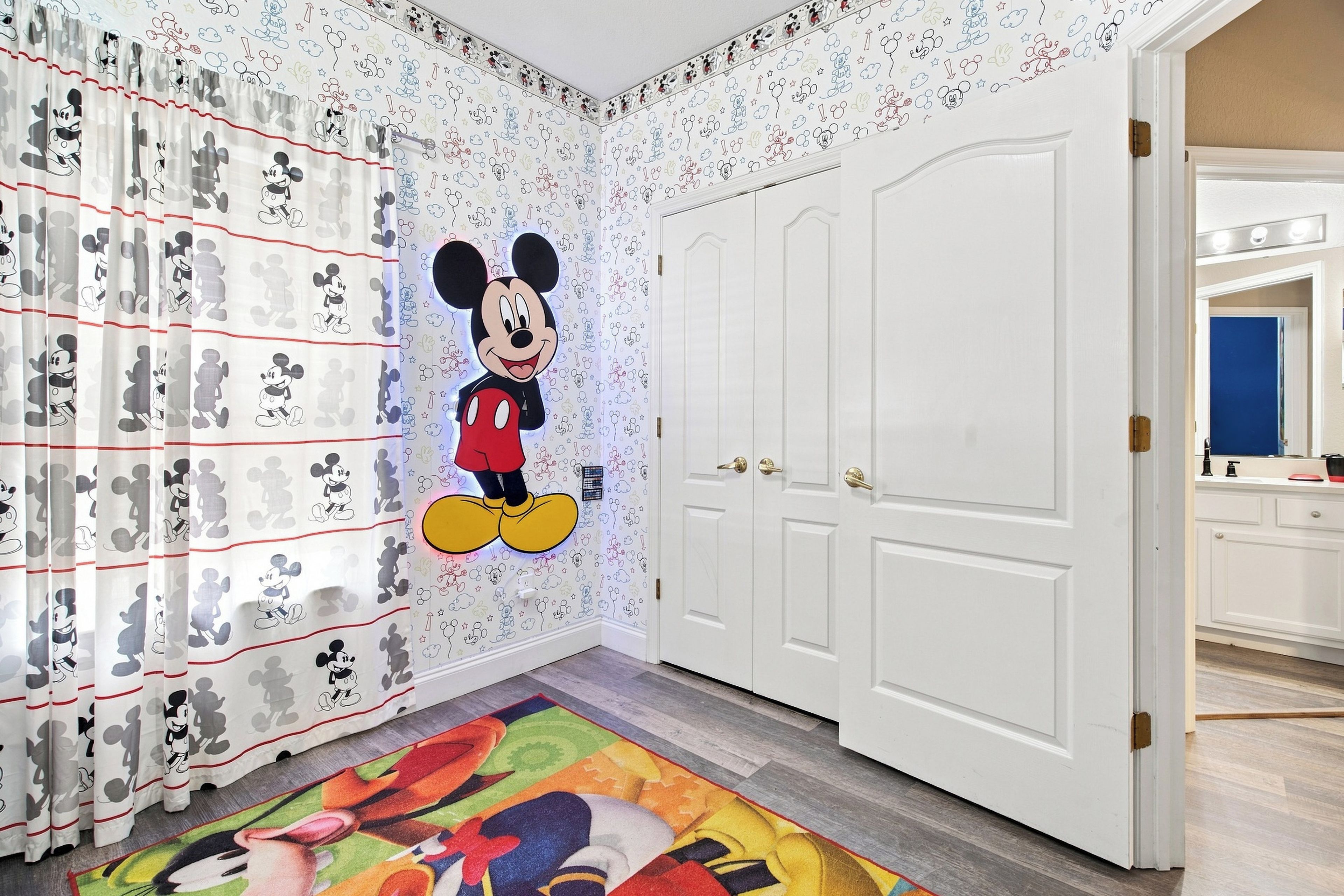 Ein Zimmer mit Wandmalerei von Mickey Mouse, weißen Türen und einem farbenfrohen Teppich.