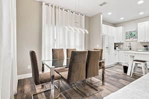 A modern kitchen with white cabinets, a stainless steel refrigerator, and a dining area with a glass table and brown chairs. - Star Wars & Mickey Kids Rooms | 18 Min to Disney (Kissimmee)