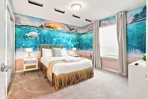 Une chambre à coucher ornée d’une fresque représentant un paysage sous-marin, un lit recouvert d’une courtepointe blanche, deux tables de chevet avec des lampes et une fenêtre avec des rideaux.