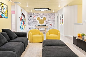 A room with two black sofas, two yellow armchairs, a Mickey Mouse mural, and a comic strip wall. - Kids Slide Room, Arcade & Game Room, Sleeps 24 (Clermont)