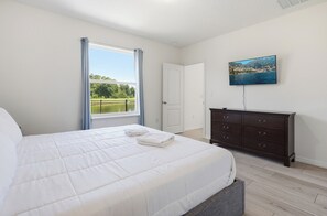 Een slaapkamer met een groot bed, een dressoir, een schilderij en een raam met uitzicht op groen.