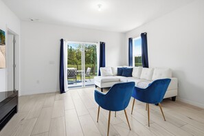 Een moderne woonkamer met een witte bank, twee blauwe fauteuils en een glazen schuindeur naar een balkon.