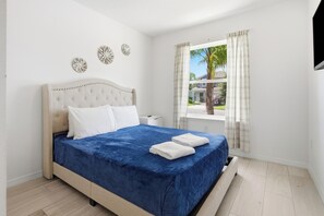 A bedroom with a bed, white walls, a window with curtains, and a view of a palm tree. - Super Mario Room & Lake View Patio, Sleeps 8 (Kissimmee)