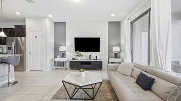 Un salon moderne avec un canapé, une table basse et un téléviseur. Il y a également un coin cuisine équipé d’un réfrigérateur et de placards.