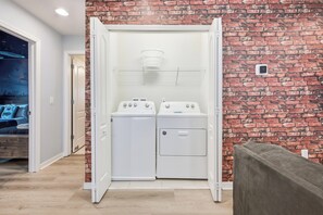Une buanderie avec un mur en briques, deux machines à laver et un sèche-linge.