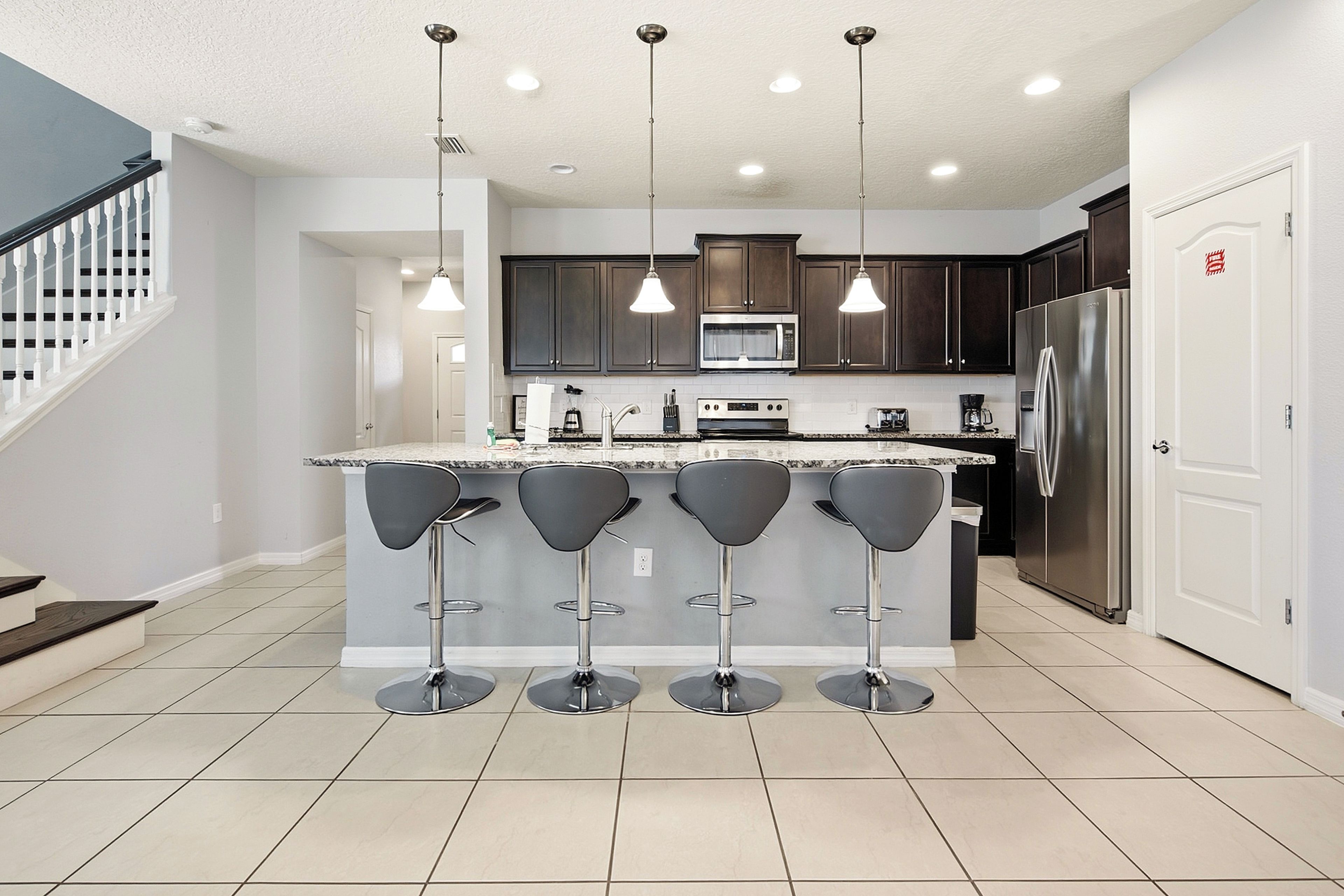 Une cuisine moderne dotée d’un îlot central, de tabourets de bar, d’appareils électroménagers en acier inoxydable et de luminaires suspendus.