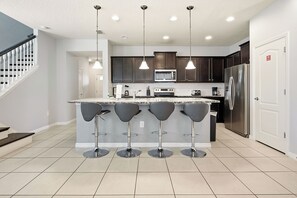 Une cuisine moderne dotée d’un îlot central, de tabourets de bar, d’appareils électroménagers en acier inoxydable et de luminaires suspendus.
