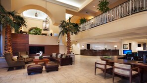 Eine großzügige Lobby mit hoher Decke, einem Empfangstresen, Sitzbereichen und einer Treppe.