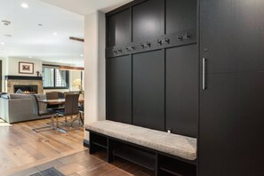 Sala de estar moderna com lareira, área de jantar e um banco encostado em parede escura com ganchos.
