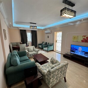 A living room with a flat-screen TV, green sofas, a coffee table, and a ceiling light fixture. - 2-bedroom apartment in marvelous Giza with AC for relaxing stays (Giza)