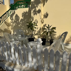 A white picket fence, two potted plants, and a plastic chair in a sunny outdoor area. - 2-bedroom apartment in marvelous Giza with AC for relaxing stays (Giza)