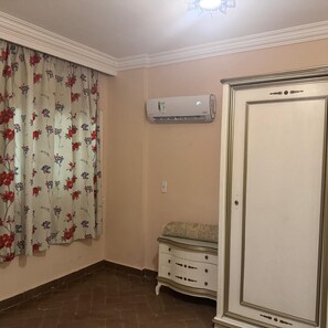 Ein Zimmer mit einem blumigen Vorhang, einer Klimaanlage, einem weißen Schrank und einem gefliesten Boden.