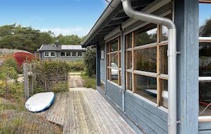 Eine Holzterrasse mit einem Surfbrett, ein Haus mit großen Fenstern und eine Solaranlage.