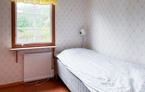 Ein kleines Zimmer mit einem Einzelbett, einem Fenster, einer Heizung und Wandtapete mit Muster.