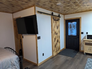 Ein Zimmer mit einer Schiebetür, einem Wandfernseher, einem Bett und einem kleinen Schrank.