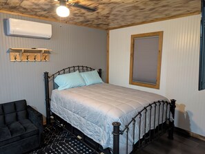 A bedroom with a bed, a chair, a wall-mounted air conditioner, and a ceiling fan. - Cabin Harper, 1-bedroom cabin in the heart of Amish Country in charming Clare (Clare)