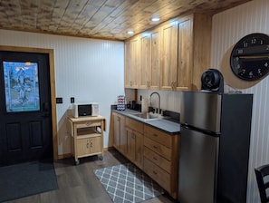 Eine Küche mit Holzausstattung, einem Edelstahlkühlschrank, einer Mikrowelle auf einem Holzwagen und einer Wanduhr.