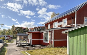 En röd byggnad med en grön dörr, en trappa och en parkeringsplats.