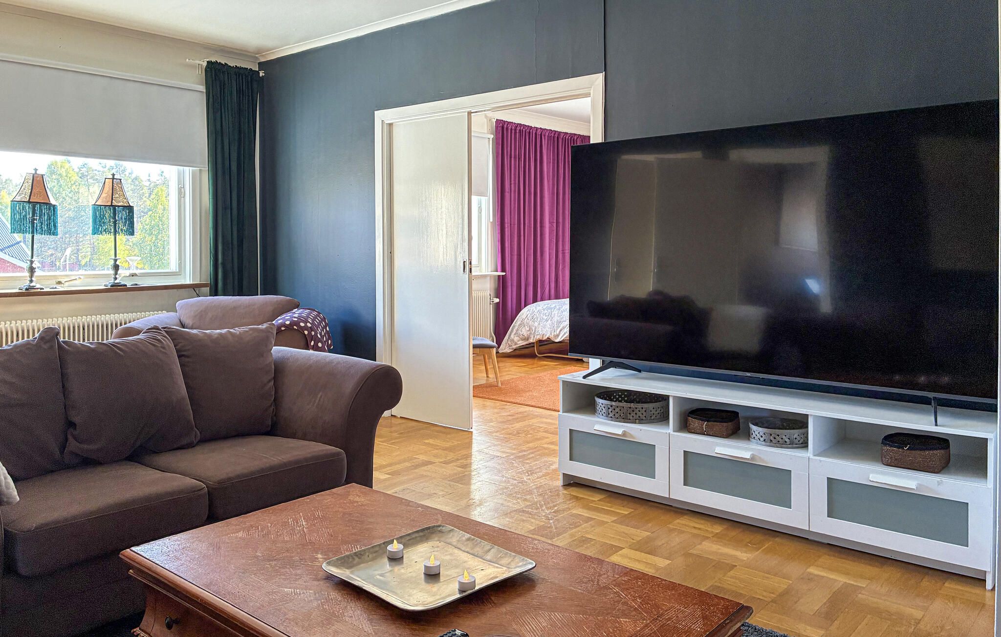 A living room with a sofa, a coffee table, a TV on a stand, and a window with curtains.