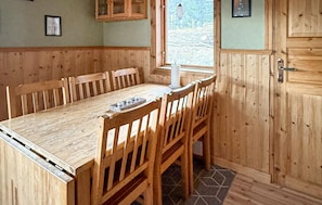 A wooden dining table with chairs, a window with a view of a garden, and wooden walls.