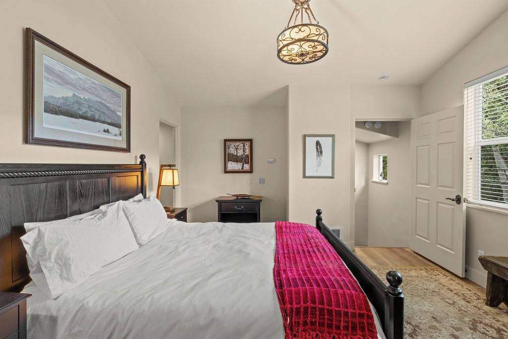 A bedroom with a bed, a nightstand, a lamp, a framed picture on the wall, and a door leading to another room.