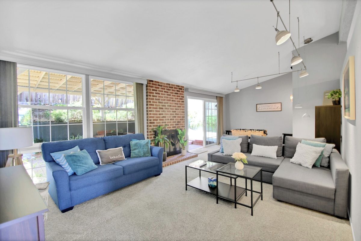 A modern living room with a blue sofa, a grey sofa, and a coffee table. There is a brick wall and large windows.