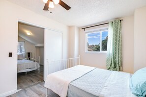 Een slaapkamer met een bed, een plafondventilator, een raam met gordijnen en uitzicht op de omgeving.