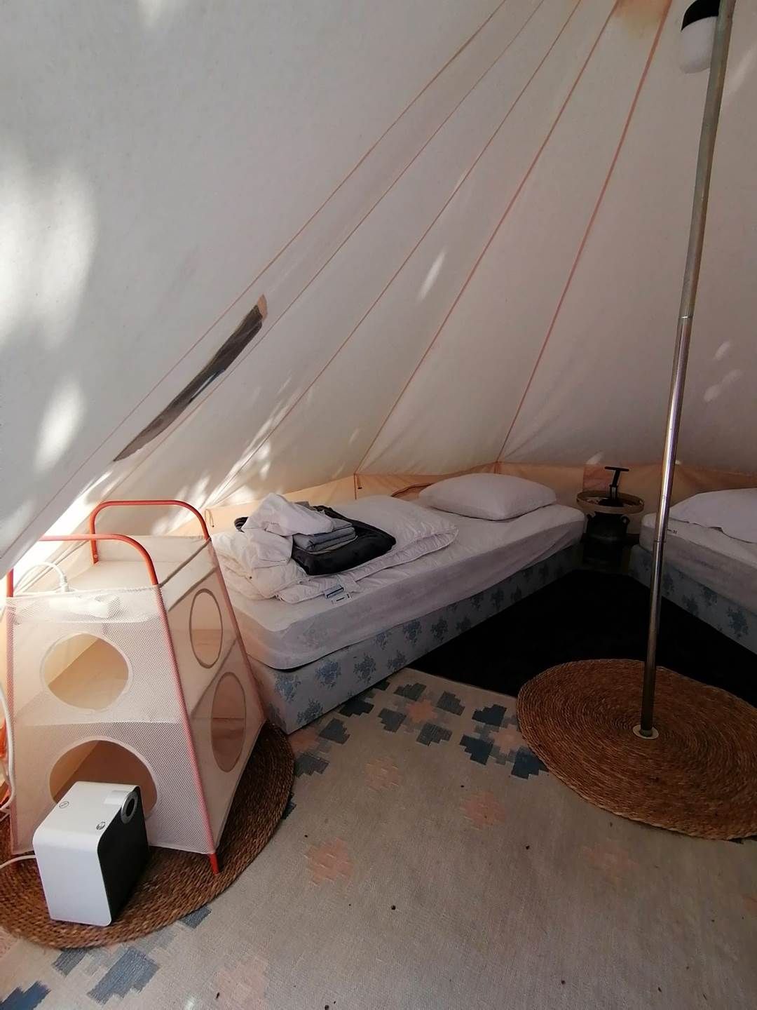 A tent with a bed, a small table, and a portable speaker.