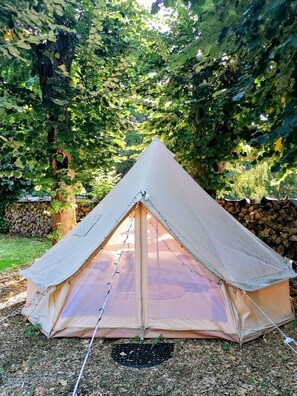 Een tent met een driehoekige vorm opgezet in een tuin, met bomen en een stenen muur op de achtergrond.