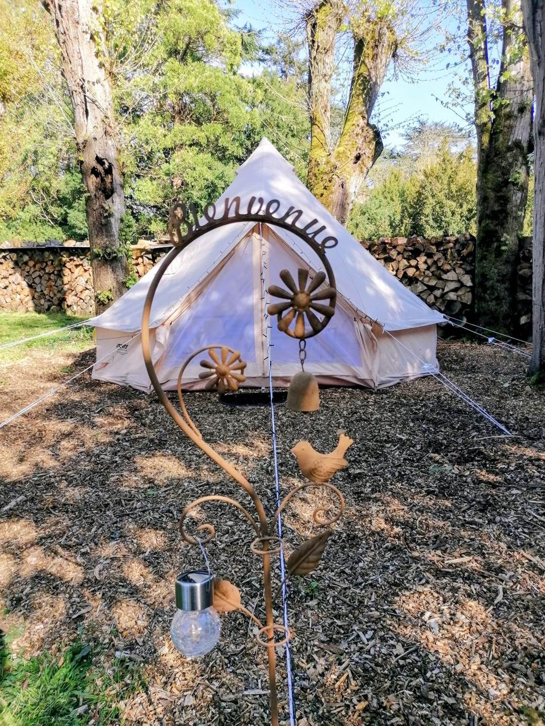 Een tent met 'Bienvenue' erop, omringd door een decoratieve metalen constructie met een vogel en een lamp.