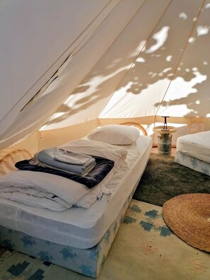Een tent met een bed, een tafeltje en een geweven mat.