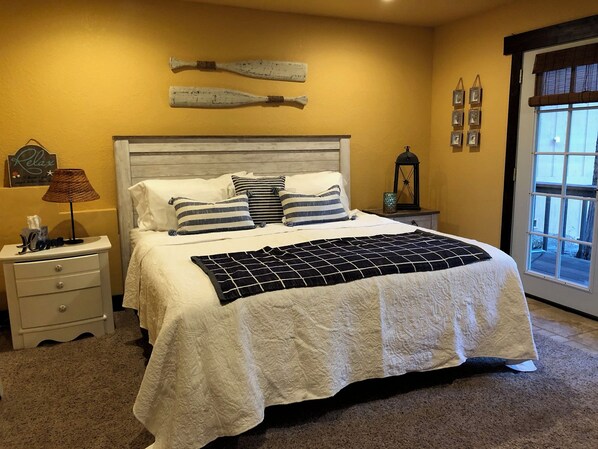 A bedroom with a large bed, a nightstand, a lamp, and a window with blinds.