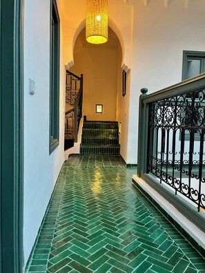 A hallway with green patterned flooring, a staircase with a railing, and a light fixture above. - Riad – Heated Pool & Rooftop in the Heart of the Medina (Marrakech)