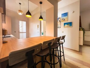 Une cuisine moderne avec un îlot central en bois, des tabourets de bar, des luminaires suspendus et des œuvres d’art accrochées aux murs.
