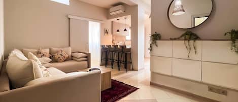 A modern living room with a sofa, a dining area with chairs, and a kitchen in the background.