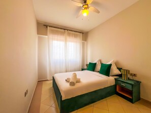 Ein Hotelzimmer mit Bett, Nachttisch, Deckenventilator und einem Fenster mit Vorhängen.